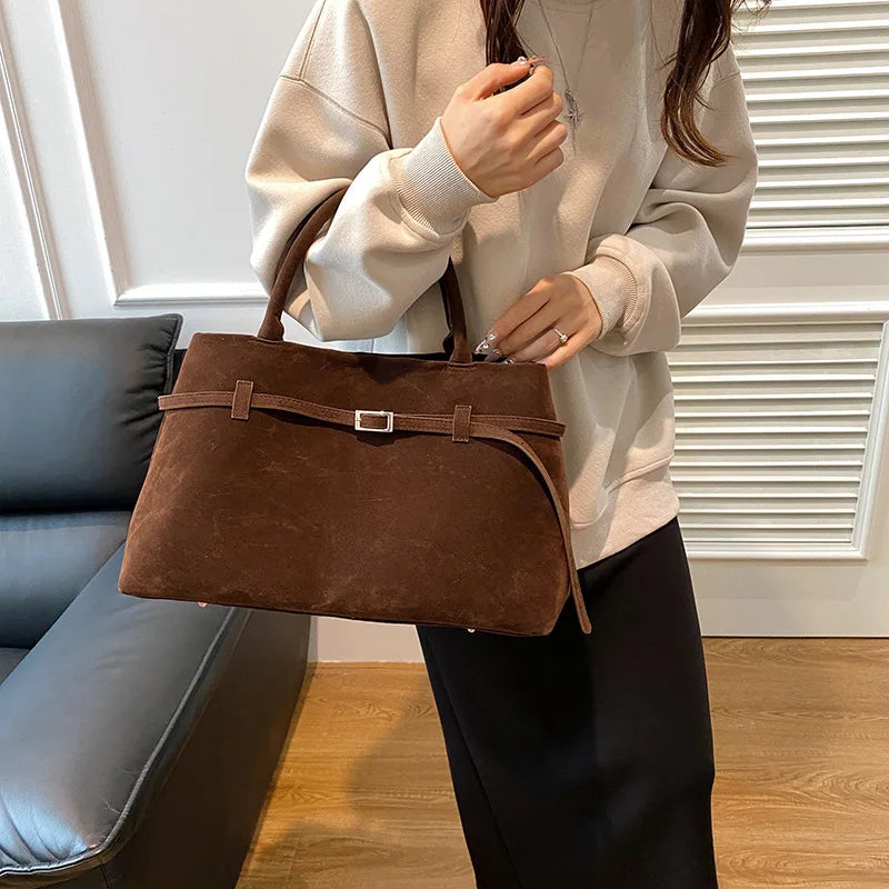 Sac à main KELLY en daim couleur café avec bandoulière, élégant et léger, parfait pour un style féminin et chic au quotidien, porté main, vue de face.